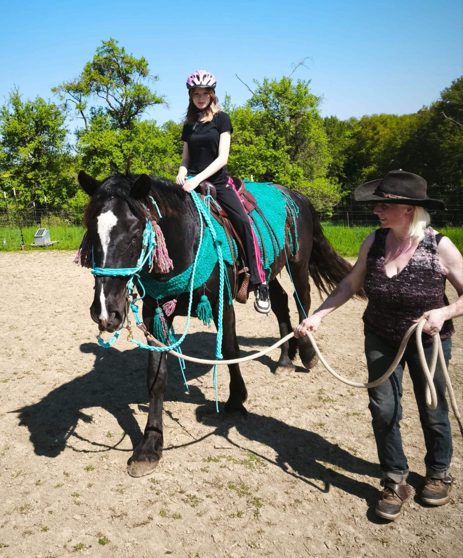 Eine Person geht neben einem jungen Pferd namens Thor her, das ein Kind auf dem Rücken trägt. Das Pferd befindet sich noch in der Ausbildung für die spätere therapeutische Arbeit. Die Szene findet im Freien statt und wirkt ruhig und sicher.