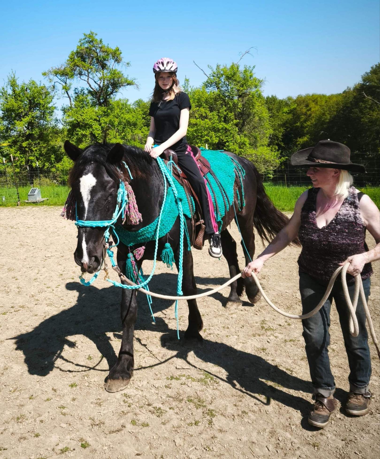 Eine Person geht neben einem jungen Pferd namens Thor her, das ein Kind auf dem Rücken trägt. Das Pferd befindet sich noch in der Ausbildung für die spätere therapeutische Arbeit. Die Szene findet im Freien statt und wirkt ruhig und sicher.